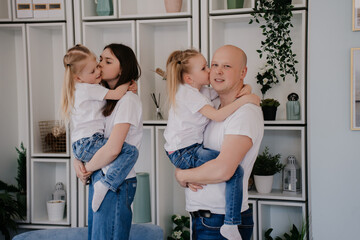 Father with daughters at home kissing each other, dressed in white t-shirts and blue denim jeans. Playful family at home preparing to spend weekend together. Fatherhood and family concept.