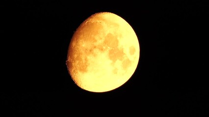 Wall Mural - A glowing golden huge moon seen from earth through the atmosphere against a starry night sky. A large moon moves across the sky, the moon moving from the left frame to the right.