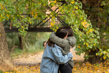 Two Female Friends Embracing In A Park On A Autumn Day. 