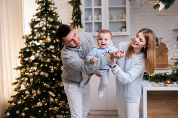 A happy family. Happy young couple with their little son in the kitchen decorated for the new year. New Year's interior in the kitchen. Christmas kitchen. Festive family atmosphere.