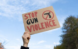 Fototapeta Mapy - Hand holding a sign with slogan Stop Gun Violence and black pistol strikethrough. Woman with placard at protest rally demonstration strike to ban weapons and end shooting.