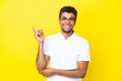 Young handsome Brazilian man isolated on yellow background happy and pointing up