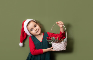 Wall Mural - Cute caucasian kid toddler girl in red Santa's hat holds festively decorated basket on red background. Copy space for design or text. Banner. Christmas New Year mockup template.