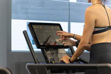 Wall Mural - Girl Touching a Display of Modern Treadmill in Fitness Club during her Workout in Fitness Club