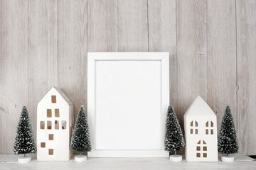 Wall Mural - Christmas mock up with white frame, white houses and tree decor. Portrait frame on a wood shelf against a rustic grey wood wall panel background. Copy space.