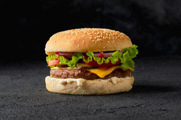 Wall Mural - Classic traditional cheeseburger with beef, tomato, lettuce, pickles and onion on black background