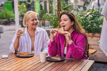 Positive woman eating with appetite her sandwich meal while sitting at the street cafe