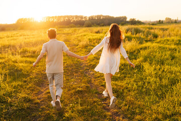 Wall Mural - back view of unrecognizable happy young couple in love taking each other hand and walking in meadow 