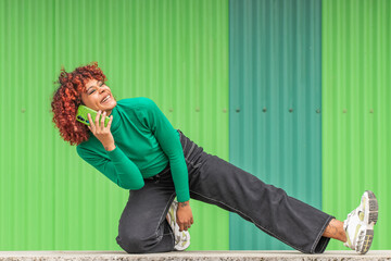 latin afro american girl smiling out loud talking on mobile phone in green urban background