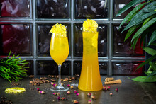 homemade lemonade with the taste of tropical fruits in a glass or decanter. Lemonade with ice in a yellow glass. Lemonade is decorated with pineapple slices and stands on a decorated table.