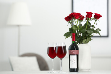 Sticker - Bottle, glasses of red wine and vase with roses on table in room, space for text. Romantic date