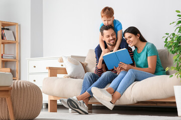 Canvas Print - Happy family reading book together on sofa in living room at home