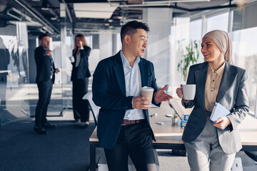 Wall Mural - Two happy multiracial colleagues talking and drinking coffee during break time in office