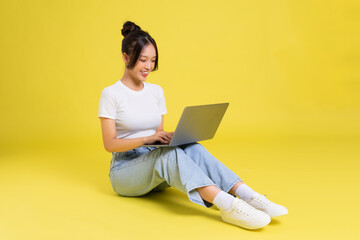 Wall Mural - portrait of a beautiful young asian girl sitting on a yellow background