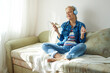 © evafesenuk - Senior woman sitting on sofa wearing headphones listening to music