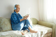 © evafesenuk - Mature woman sitting on the couch with headphones listening to music or audio book