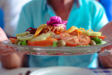 Mature Man With Turquoise Shirt Holds A Plate Of Inviting Fresh Mixed Salad With Fruit And Vegetables. Concept Of Healthy, Vegetarian And Vegan Eating