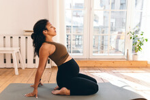 Pregnant african american woman in crop top and leggings sitting on her heels, leaning back on hands, looking up, doing prenatal yoga to keep fit and preparing her body for childbirth