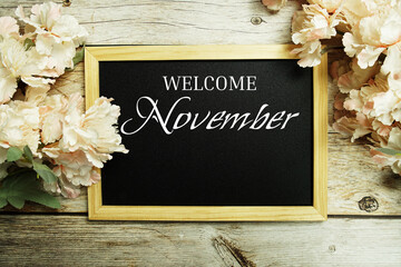 Canvas Print - Welcome November text message on blackboard with flower decoration on wooden background