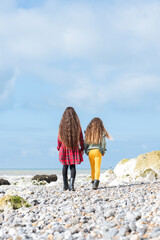 Wall Mural - Back view of two little girls in red tartan dress, green jumper and yellow leggings walking at Hope Gap beach near Cuckmere Haven located between Seaford and Eastbourne in East Sussex, UK