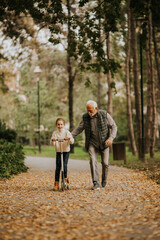 Wall Mural - Senior man teaching his granddaughter how to ride kick scooter in park