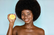 © Beauty Agent Studio - Organic cosmetic concept. Beauty portrait of Overjoyed African american model holding a fresh lemon, posing against blue background.