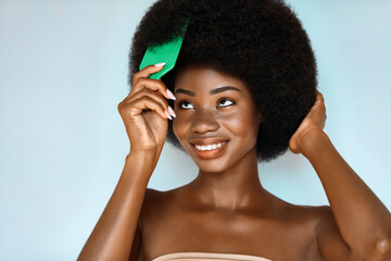 Wall Mural - curly afro hair treatment. haircare cosmetic. overjoyed african american model is brushing her hair 