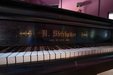 a piano with a black case and a white keyboard with writing on it and a mirror behind it in a room.