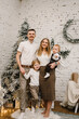 © Serhii - Merry Christmas. Happy mother, father, and kids near Christmas tree in home. Mom, dad hug children. Beautiful family enjoying their holiday time together and having fun. Decorated interior of a house.