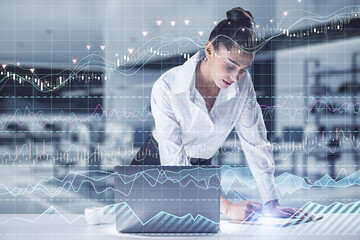 Wall Mural - businesswoman leaning and writing on desktop with laptop and candle stick grid graph chart of stock market investment trading. Bullish point, Bearish point and financial growth concept.