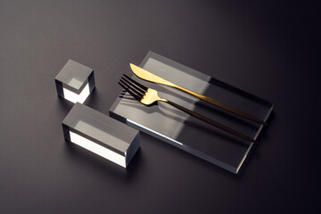 Haute cuisine concept with a golden cutlery on a glass podium on a dark background. Restaurant table setting.