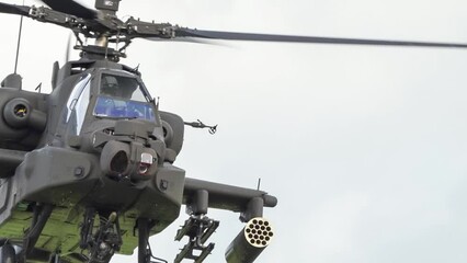 Wall Mural - detailed close-up of British army Boeing Apache Attack helicopter gunship (AH-64E AH64E) flying slow and low, a glance from pilot and gunner, before Apache descends behind bushes