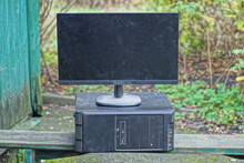 An Old Black Desktop Computer And A Large Dirty Monitor Stand On A Gray Wooden Table On The Street Against The Backdrop Of Green Vegetation