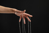 Fototapeta Konie - Woman pulling strings of puppet on black background, closeup