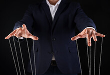 Man In Suit Pulling Strings Of Puppet On Black Background, Closeup