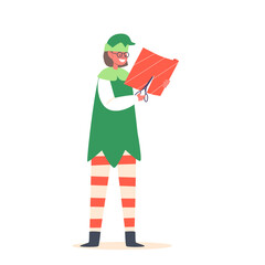 Wall Mural - Cute Playful Christmas Elf Cutting Paper For Wrapping Gifts. Funny Santa Claus Helper In Green Costume And Stockings