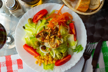 Plate of low calorie traditional Spanish salad with goat cheese, fresh tomatoes, lettuce olive and canned corn