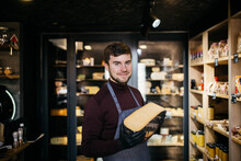Portrait Of Handsome Bearded Man Sniffing Old Cheese In Shop.