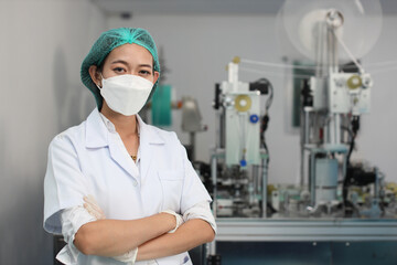 Poster - Worker in personal protective equipment or PPE inspection quality crossed arms and looking camera in mask and medical face mask production line factory, manufacturing industry and factory concept.