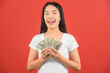 © Johnstocker - Portrait of a cheerful young woman holding money banknotes and celebrating isolated over red background