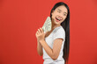 © Johnstocker - Portrait of a cheerful young woman holding money banknotes and celebrating isolated over red background