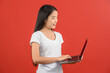 © Johnstocker - Portrait of a happy asian businesswoman working on laptop computer isolated over red background