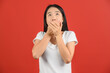 © Johnstocker - Portrait of Surprised young asian woman in white t-shirt looking up and hands cover mouth isolated on red background