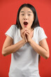 © Johnstocker - Portrait of Excited young asian woman in white t-shirt holding hands isolated on red background
