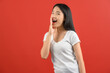 © Johnstocker - Portrait of Young asian woman in white t-shirt shout story or making announcement isolated on red background