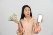 © Johnstocker - Portrait of a cheerful young woman holding money banknotes and showing smartphone mockup isolated over white background