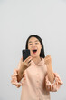 © Johnstocker - Protrait of Young asian woman expressing surprise while using mobile phone isolated over white background