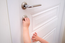 Toddler Baby Opens The Lock, Child S Hand Close-up. White Wooden Door, Metal Door Handle And Baby Hand