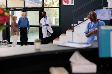 Wall Mural - African american physician explaining health care treatment to elderly couple before leaving hopsital looby. Patients having checkup visit appointment, medicine service and concept