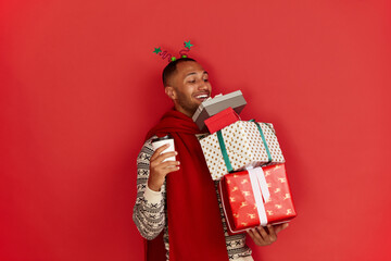 Happy Man Holding Present. Excited Multiracial Guy Holding in Coffee to Go and Wrapped Present Boxes with Excitement. New Year Concept. Indoor Studio Shot Red Background 